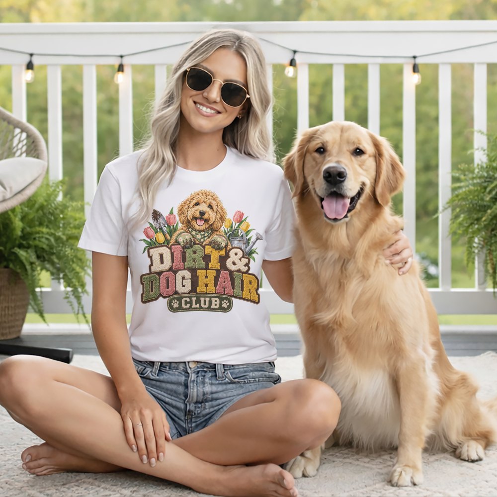 A smiling blonde woman wearing sunglasses and a Dirt and Dog Hair Club t-shirt sits with her golden retriever on a white deck.