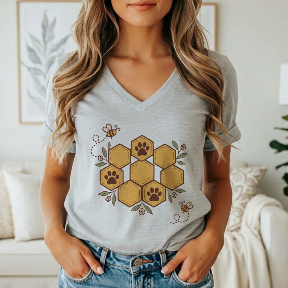 A woman wearing a gray V-neck t-shirt printed with a honeycomb and paw print graphic.