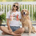 Woman in white t-shirt with cartoon dogs holding pickleballs and trophies, seated with golden retriever.