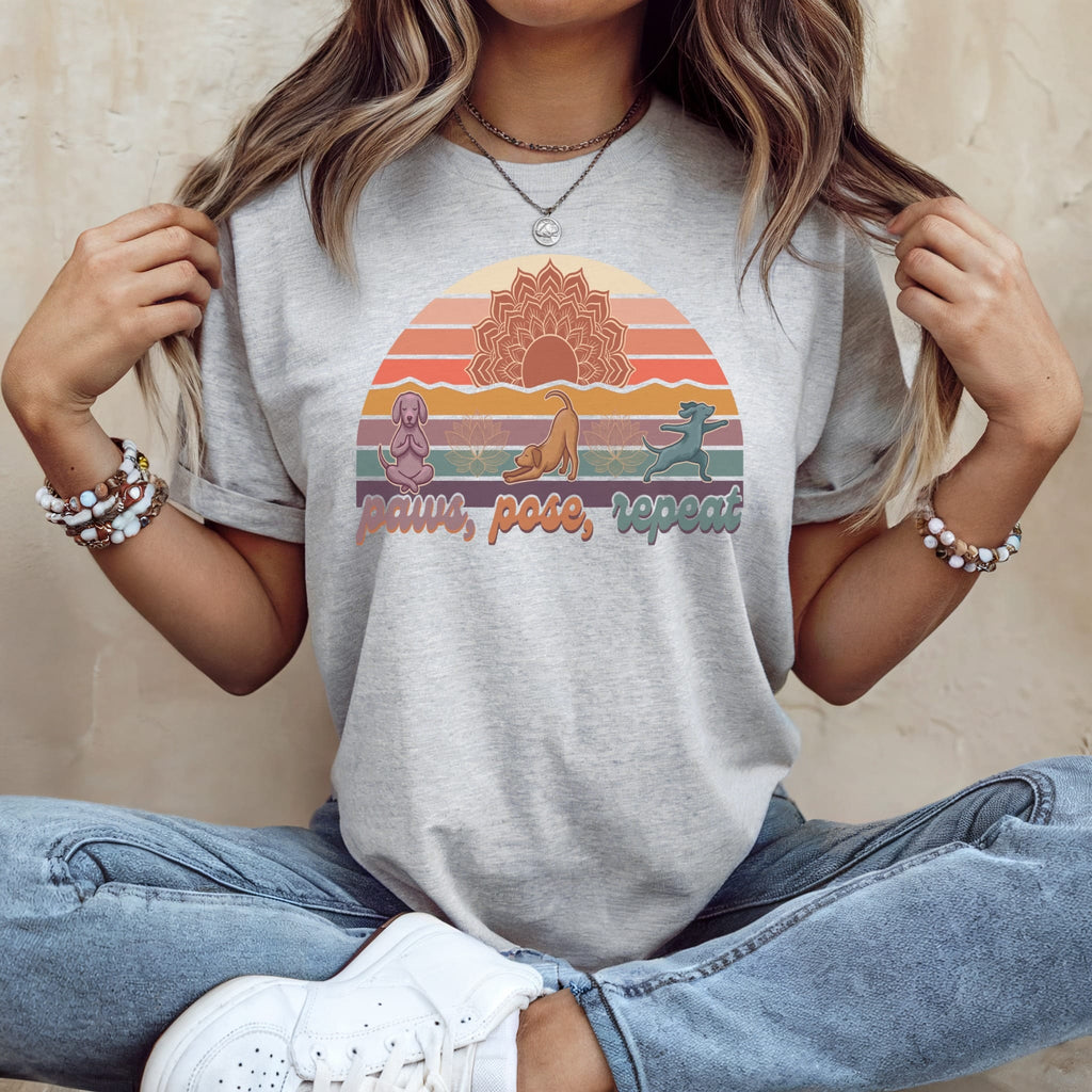 Gray t-shirt with dogs and "paws, pose, repeat" text, set against a sunset mandala.