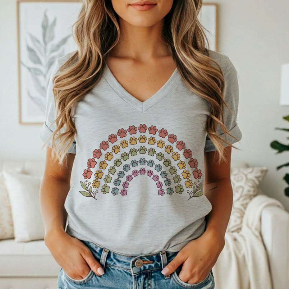 A woman wearing a grey V-neck t-shirt featuring a colorful rainbow made of paw prints.
