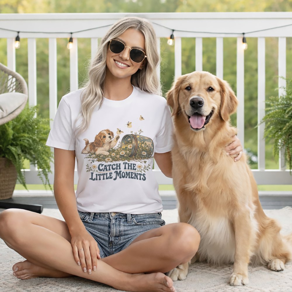 A smiling woman wearing sunglasses and a graphic t-shirt sits beside a golden retriever.