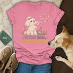 Pink t-shirt with a cartoon puppy blowing a dandelion, featuring the text Wish Big, Wag Bigger.