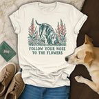 A white t-shirt featuring a dog illustration and the text "Follow your nose to the flowers."