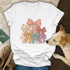 A white V-neck t-shirt featuring a pastel paw print bow graphic, displayed on a wooden surface with a dog.