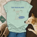 A mint green t-shirt with a graphic of a dog balancing a coffee and leash, displayed with shoes and a real dog.