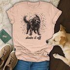 Black shaggy dog illustration with "shake it off" text on a peach t-shirt.