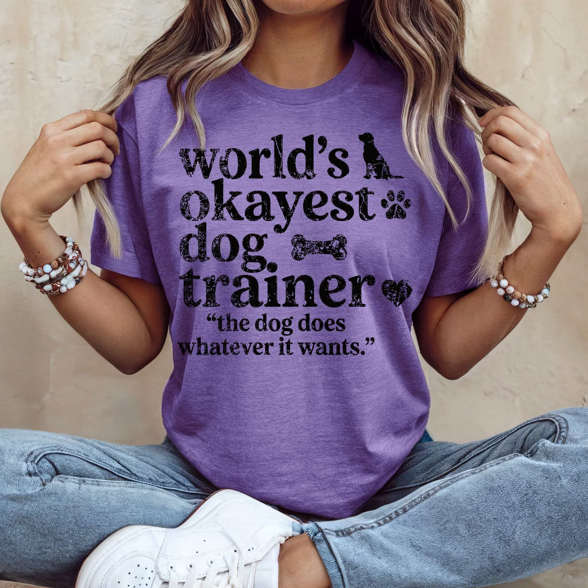 Purple t-shirt with "World's Okayest Dog Trainer" and "the dog does whatever it wants" text.