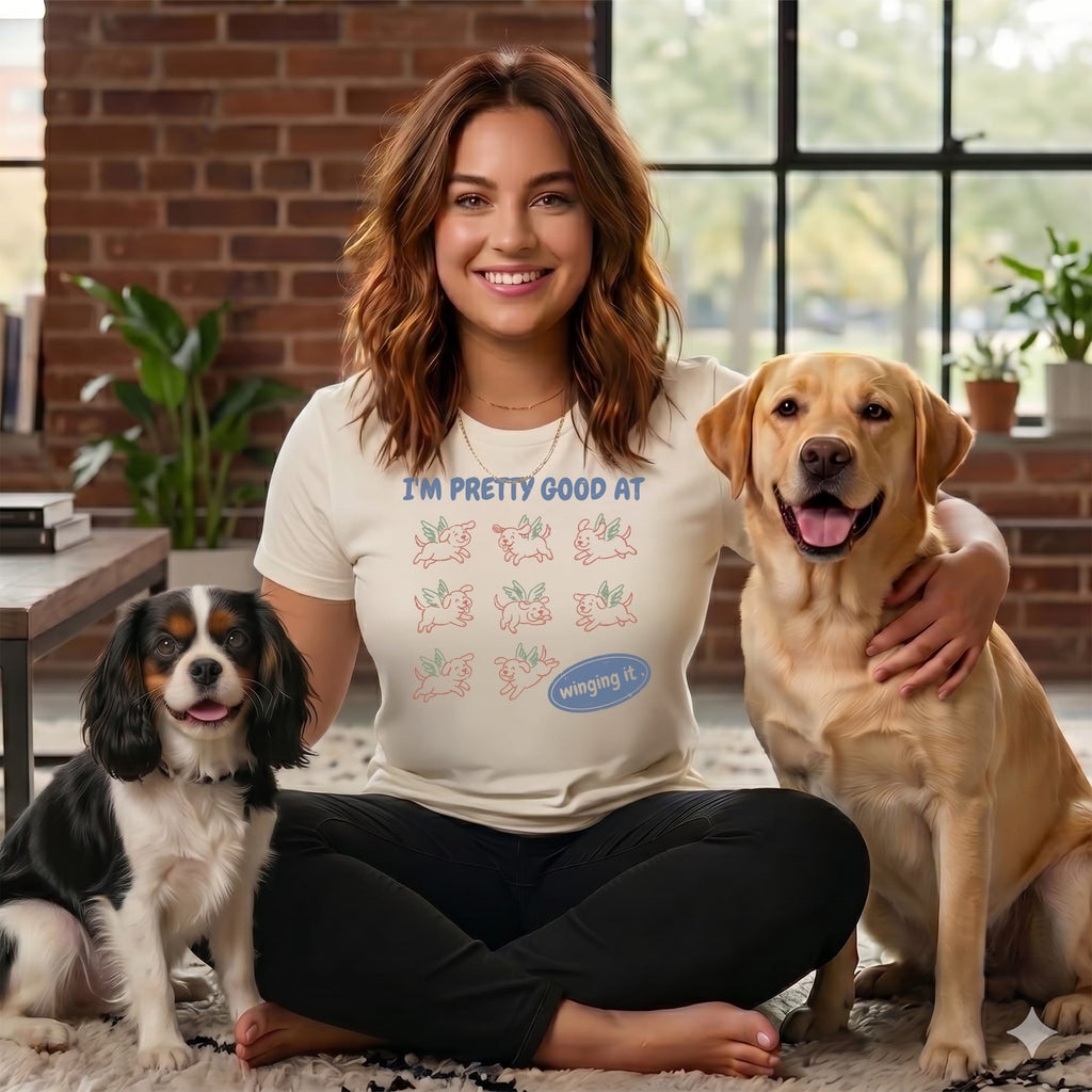 Woman in cream shirt with winged dog graphic, sitting with two dogs.