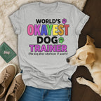 Grey t-shirt with "WORLD'S OKAYEST DOG TRAINER" text and dog paw prints.