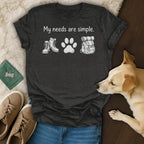 Dark t-shirt with white text "My needs are simple" above hiking boots, paw print, and backpack.
