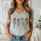 A woman wearing a gray V-neck t-shirt featuring four floral stems topped with colorful paw prints.