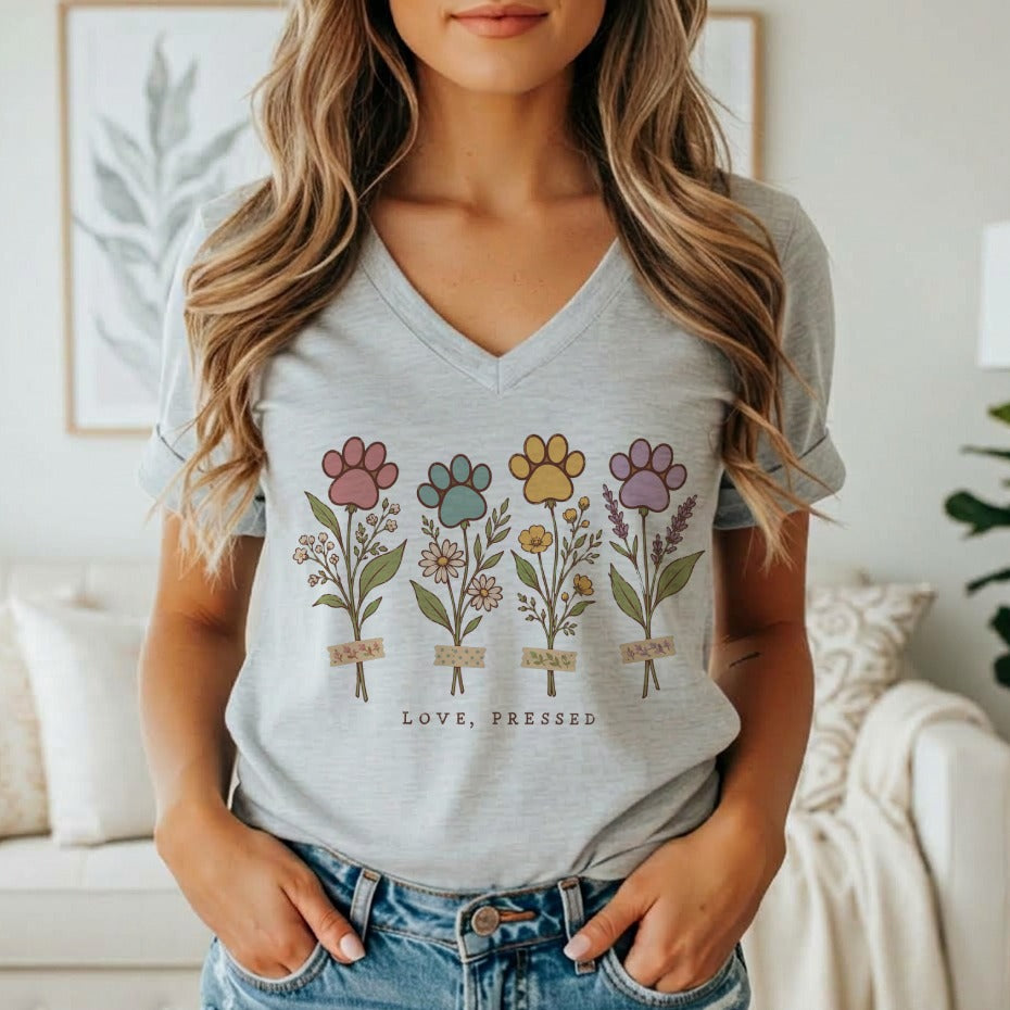 A woman wearing a gray V-neck t-shirt featuring four floral stems topped with colorful paw prints.