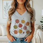 A woman wearing a gray V-neck t-shirt printed with colorful autumn leaves shaped like paw prints.