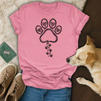 Pink t-shirt with black paw print heart design and dog beside it.