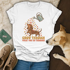 White t-shirt featuring a dachshund graphic with flowers, a watering can, and the text Grow Through What You Go Through.