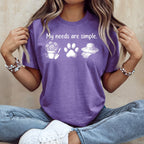 Purple t-shirt with "My needs are simple." and icons of flowers, paw print, and gardening hat.