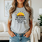 T-shirt graphic: "Watching the sunrise because someone had to pee at 5:12" with sun and dog.