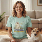 A smiling woman wearing a mint green t-shirt with a cartoon dog graphic and text reading "WISH BIG, WAG BIGGER," seated next to a small terrier.