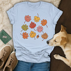 Light blue crewneck t-shirt featuring fall leaves shaped like paw prints, displayed with jeans, sneakers, and a dog.