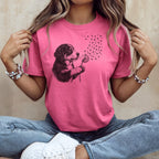 Woman wearing pink t-shirt with a drawing of a puppy blowing dandelion seeds that are paw prints.