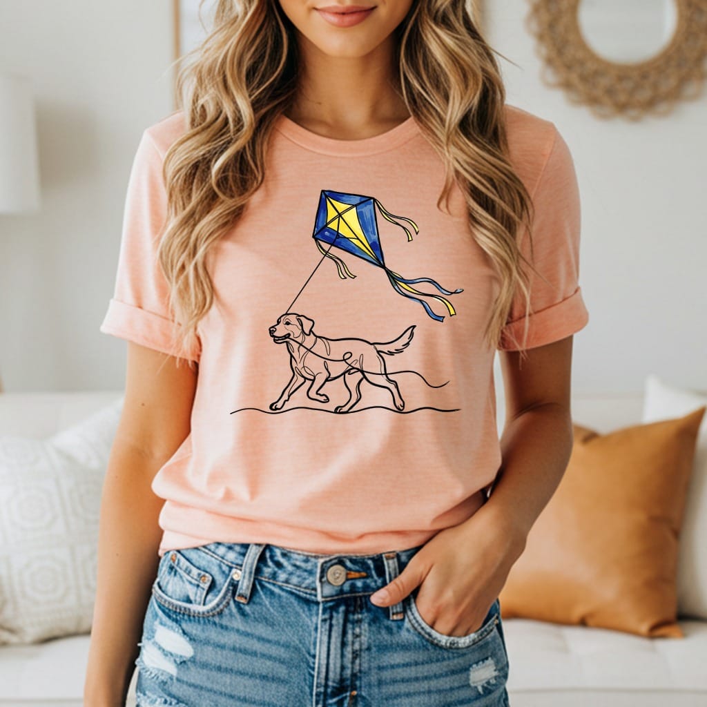 Peach t-shirt with a black line drawing of a dog flying a yellow and blue kite.