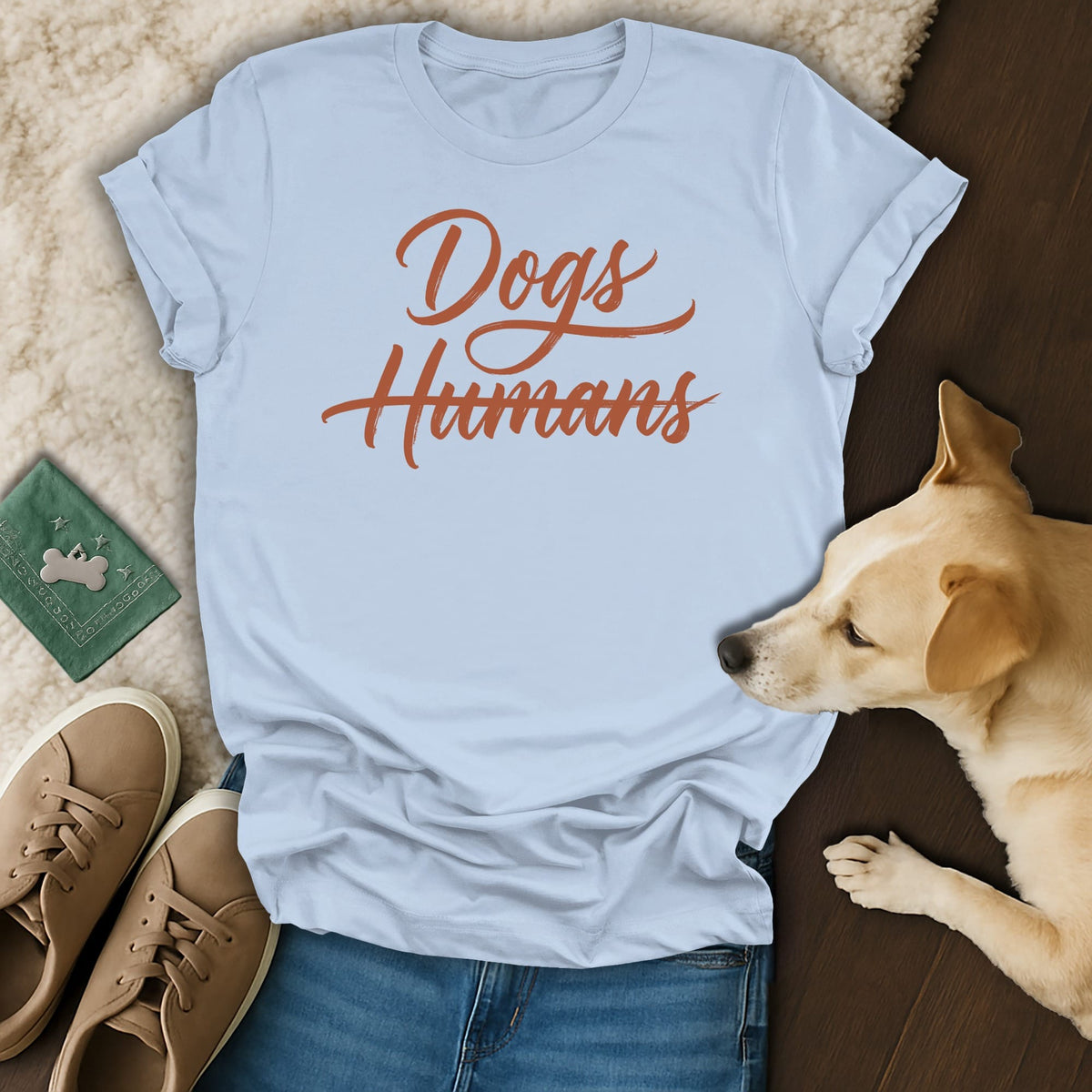 Light blue t-shirt with "Dogs Humans" text, laid flat with dog, shoes, and bandana.