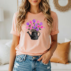 Peach t-shirt with a black watering can spilling pink and purple paw prints.
