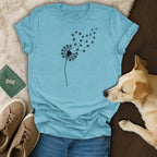 Teal t-shirt with black dandelion and paw print design, next to dog and shoes.