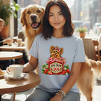 A smiling woman wears a light blue t-shirt featuring a cartoon Yorkshire terrier inside a strawberry jam jar with the text Dog Mom Is My Jam, while a golden retriever stands beside her at a cafe table.
