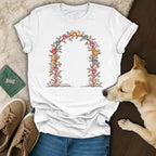 A white t-shirt featuring a floral arch and colorful paw prints graphic, accompanied by a small dog.