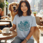 Woman with golden retriever wearing "Tidal Tails" t-shirt at cafe table.