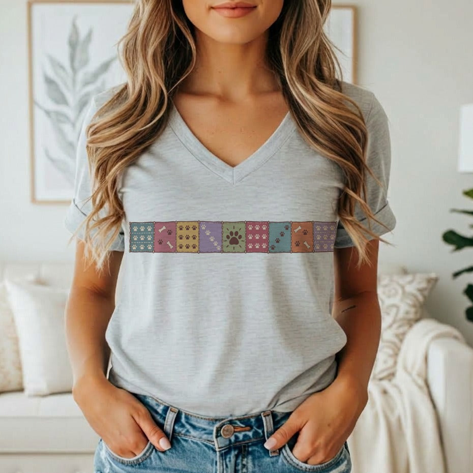A woman wearing a heather grey V-neck t-shirt with a colorful patchwork paw print graphic.