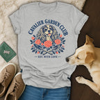 A grey t-shirt featuring a Cavalier King Charles Spaniel graphic with flowers and gardening tools.
