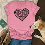 Pink t-shirt with black heart and paw prints, dog and shoes nearby.