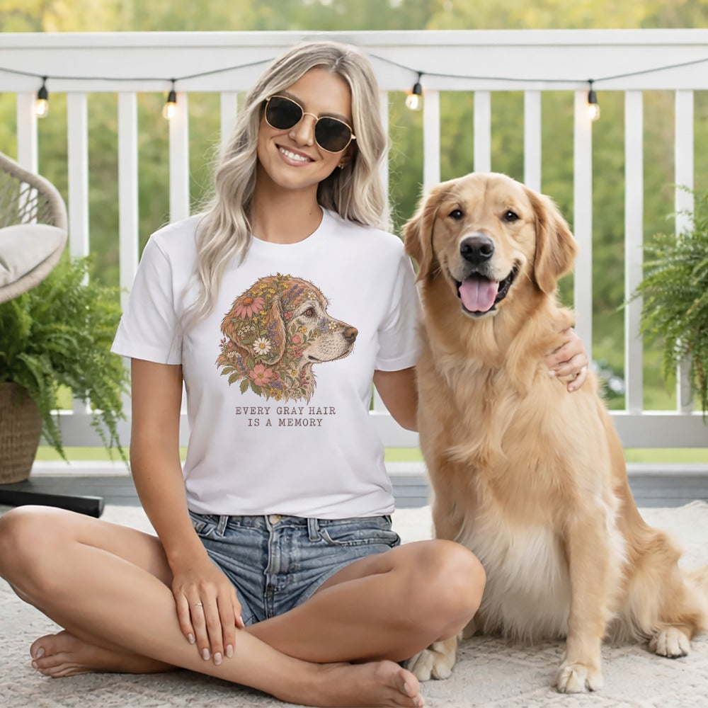 A smiling blonde woman wearing a graphic t-shirt sits outdoors next to a golden retriever.