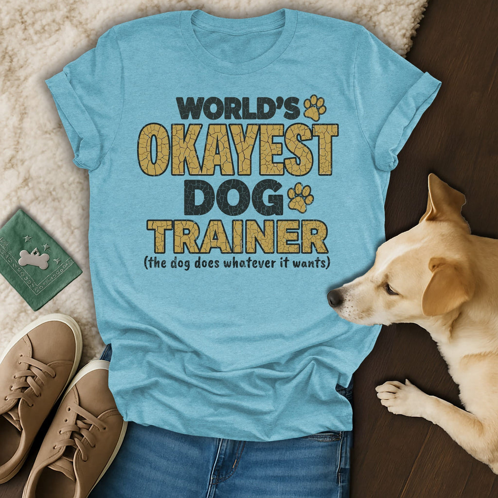 World's Okayest Dog Trainer text on a light blue t-shirt with a dog nearby.