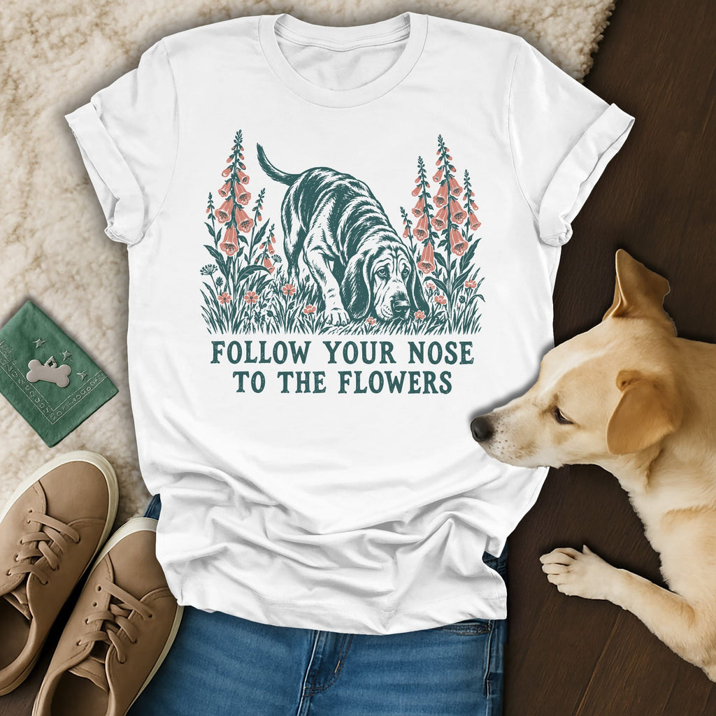 A white t-shirt featuring a hound graphic surrounded by flowers and the text Follow Your Nose to the Flowers.
