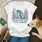 A white t-shirt featuring a hound graphic surrounded by flowers and the text Follow Your Nose to the Flowers.