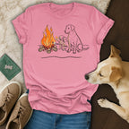 Two labrador puppies roast marshmallows by a campfire, with an adult labrador watching.