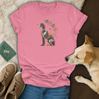 A pink t-shirt with a mosaic dog graphic is displayed with jeans, sneakers, and a sleeping dog.