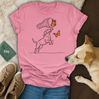 Line drawing of a dog catching butterflies with a net on a pink t-shirt.