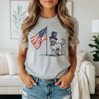 Labrador retriever wearing a patriotic hat and bow tie, standing by an American flag.