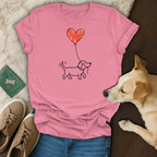 Pink t-shirt with a drawing of a dog holding a red heart balloon.