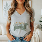 A woman wearing a heather gray V-neck t-shirt featuring a green dachshund graphic with yellow flowers and the text GROW A LITTLE EVERY DAY.