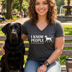 Woman with black lab on bench wearing dark grey t-shirt with white text and dog graphic.