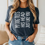 Dark grey t-shirt with white text "MY DOG TILTS HIS HEAD JUST LIKE YOU".