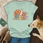 Mint green t-shirt featuring a cartoon snail graphic with paw print shells, laid out with jeans and accessories.