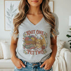 A person wearing a heather gray V-neck t-shirt with a graphic of a puppy playing with yarn and the text Knit One Pet Two.