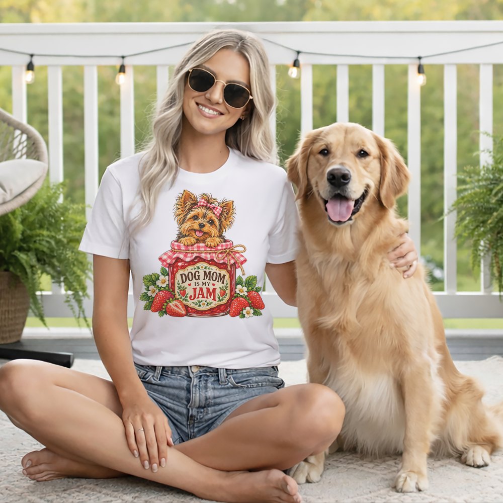 A woman wearing sunglasses and a white t-shirt that says Dog Mom Is My Jam sits next to a golden retriever on a porch.